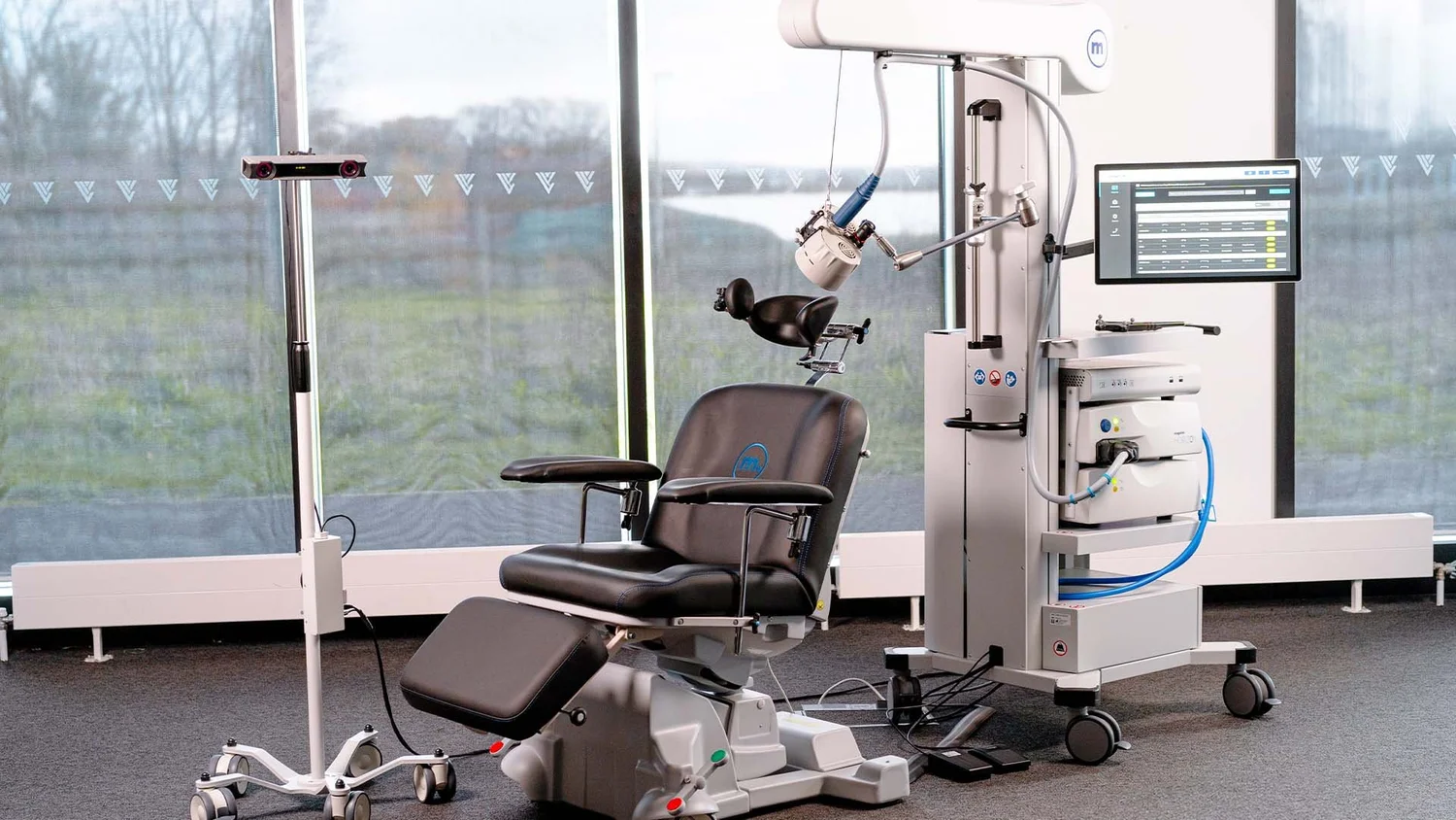 A padded TMS treatment chair with the magnetic coil arm and control unit beside a bright window
