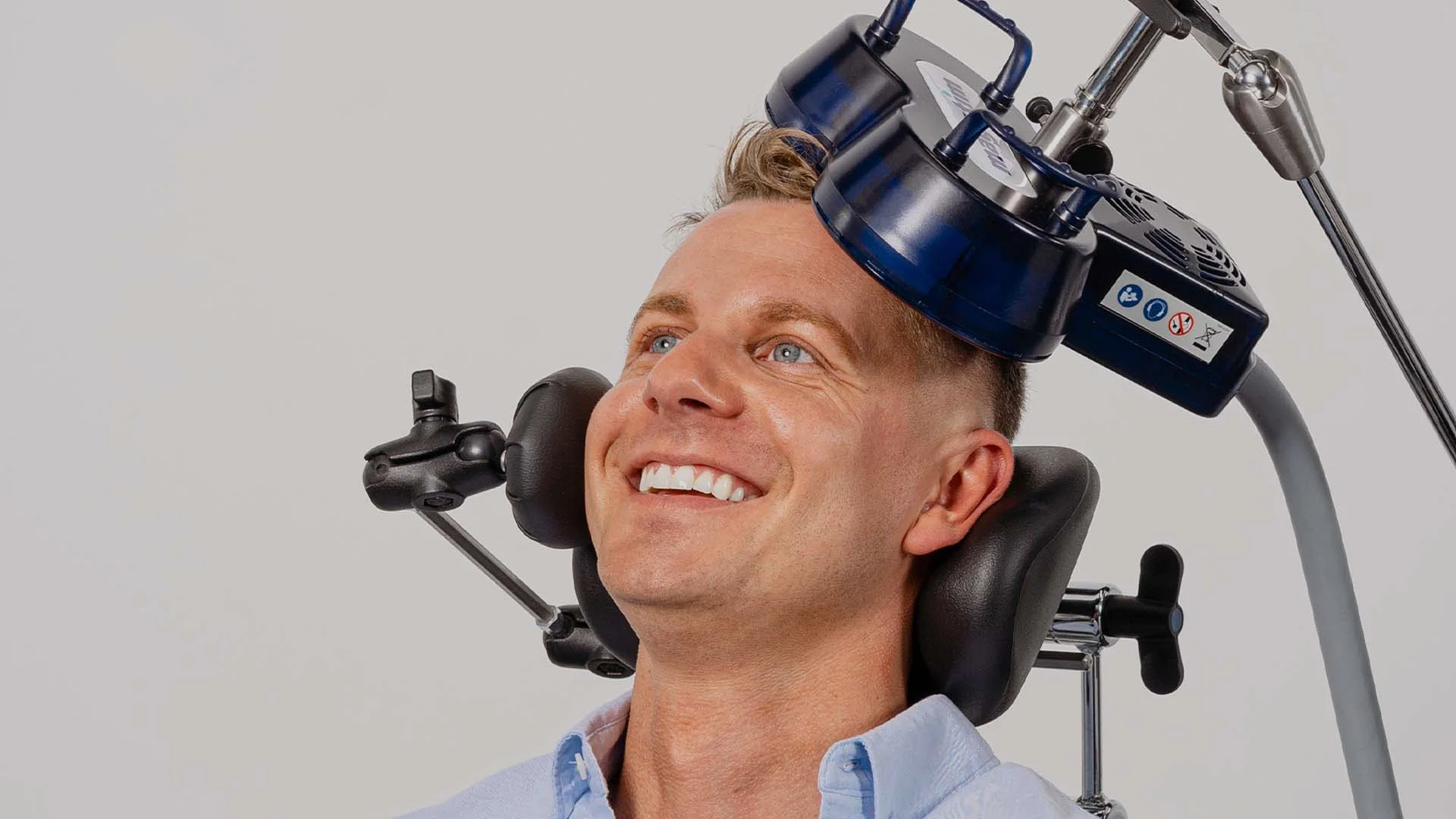 A smiling man relaxes in a padded chair during a TMS session as the Magstim Horizon coil rests against his head