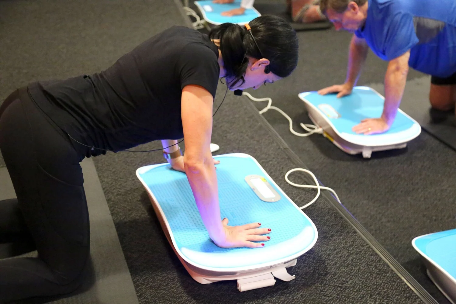 Two people doing push-ups with their hands on Wave vibration platforms during a group class